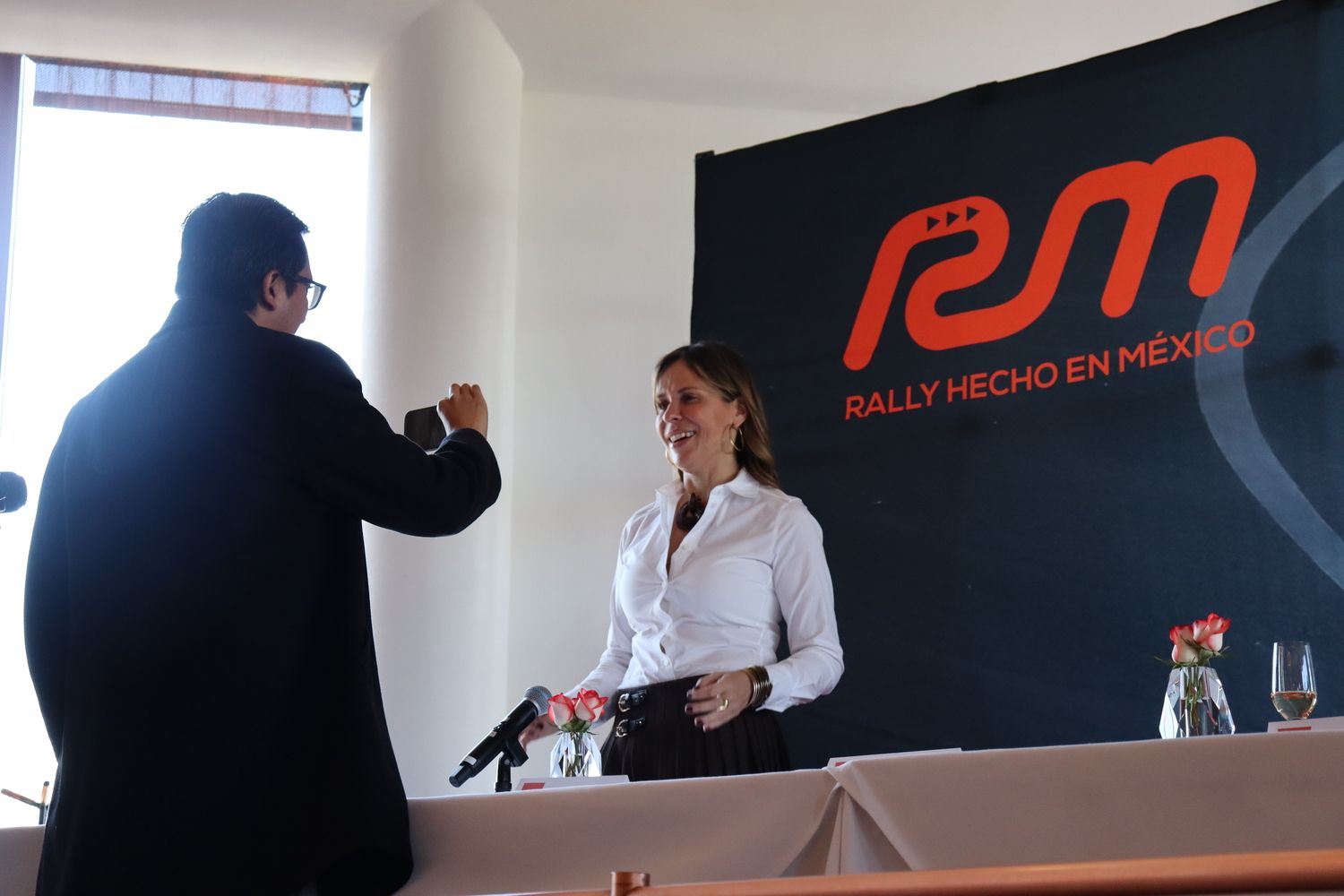 Un hombre toma una fotografía de una mujer frente a un cartel que dice rally hecho en mexico