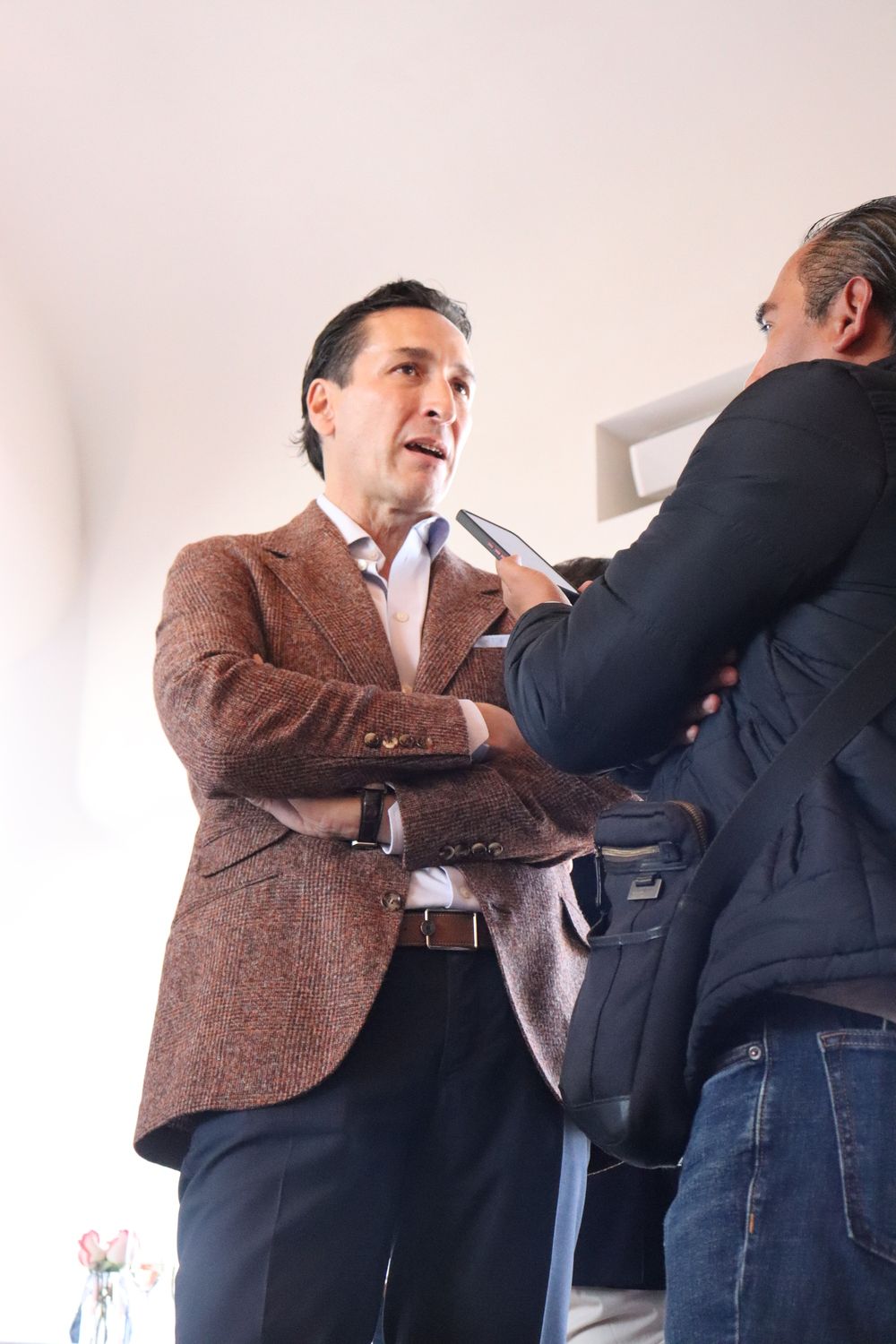 Un hombre con una chaqueta marrón está siendo entrevistado por otro hombre.