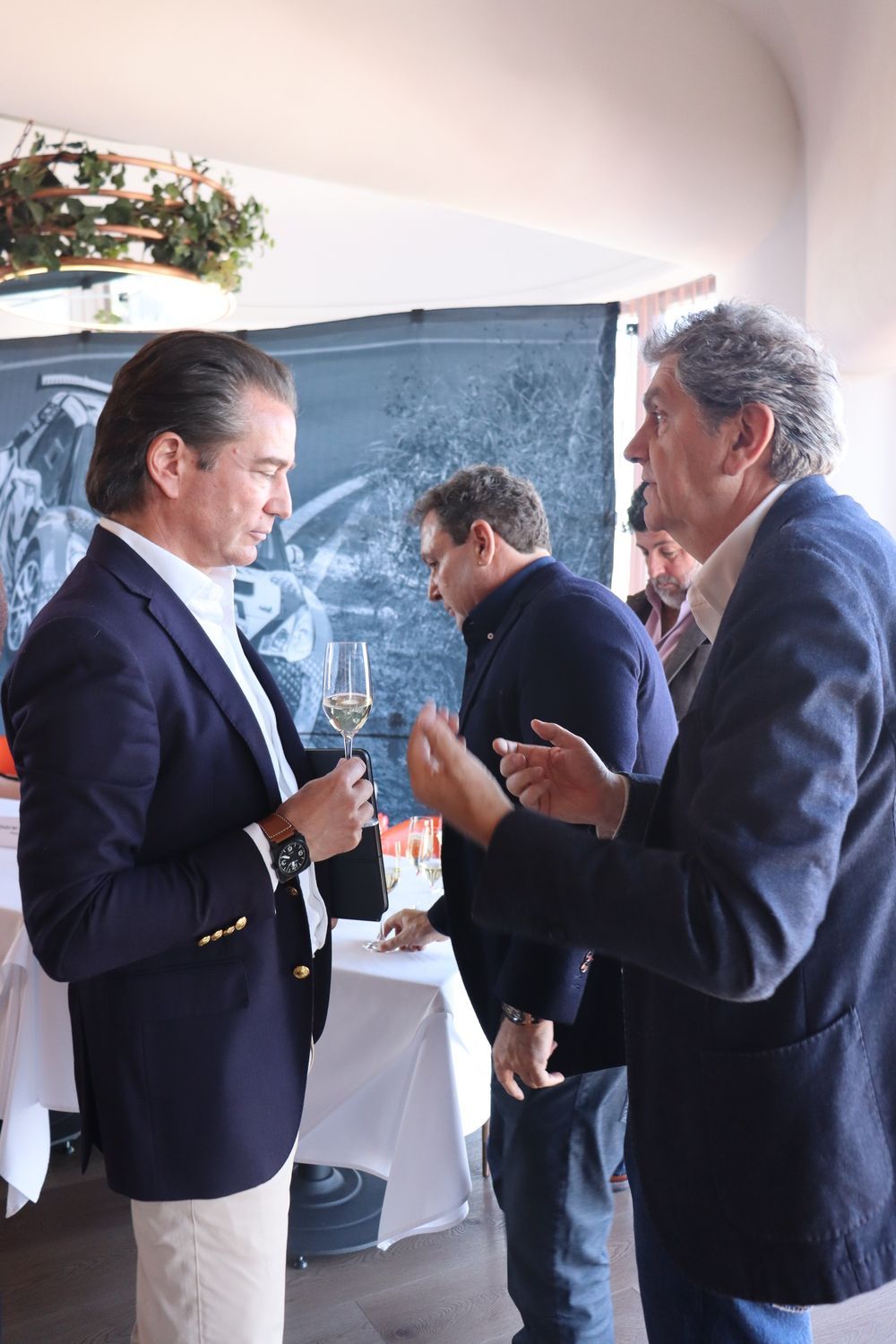 Tres hombres están uno al lado del otro hablando y bebiendo vino.