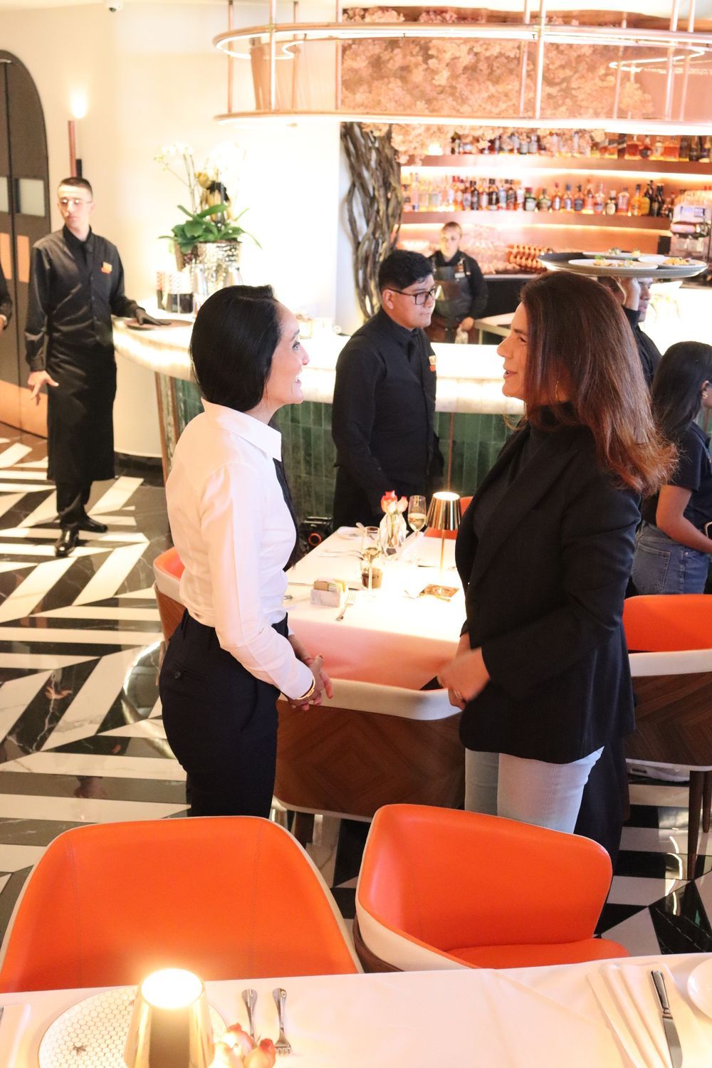 Dos mujeres están paradas en un restaurante hablando entre sí.