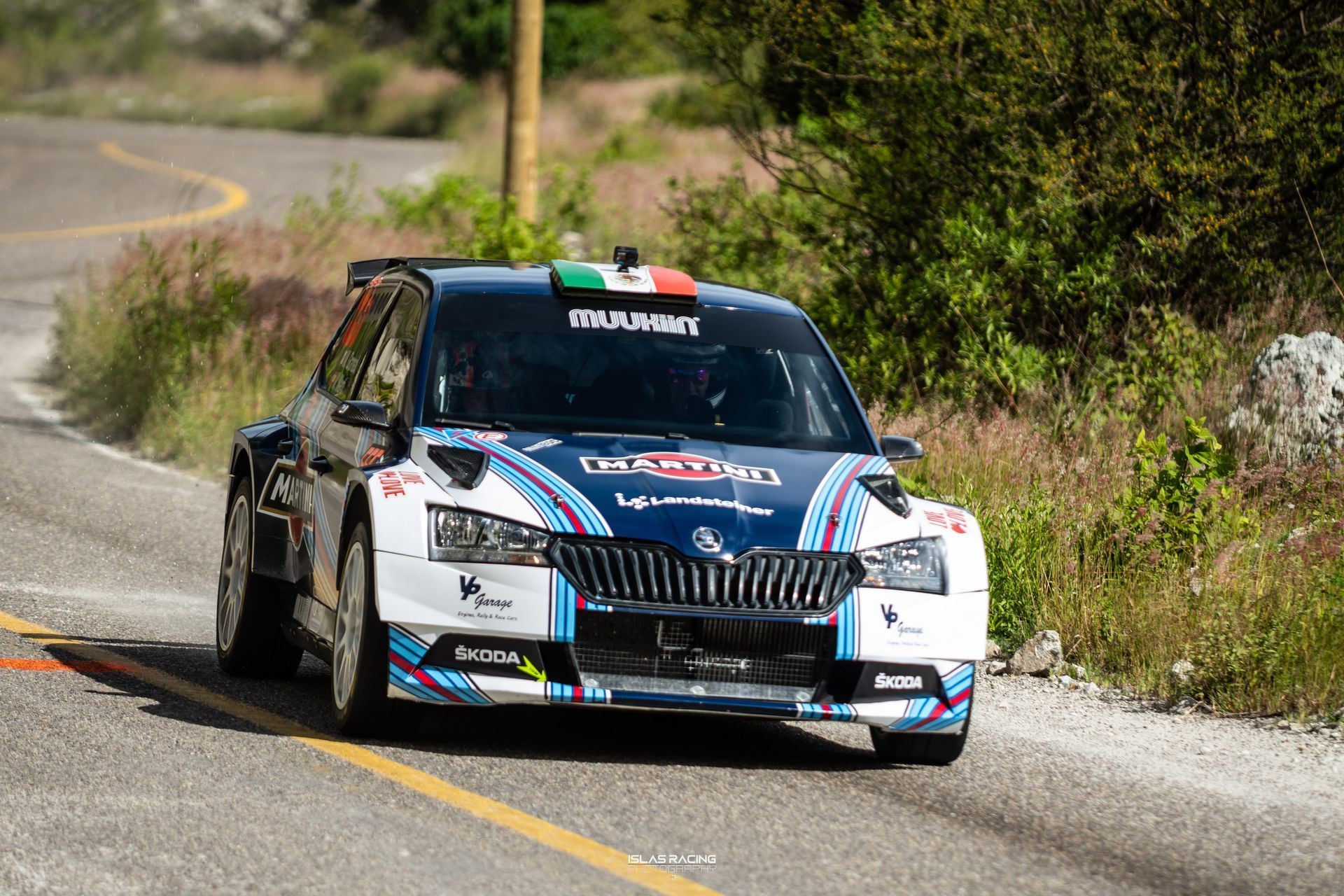 Un coche de rally azul y blanco circula por una carretera.