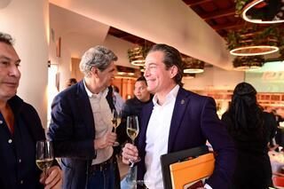 Un grupo de hombres están de pie en una habitación hablando y bebiendo vino.