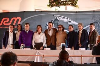 Un grupo de personas posan para una fotografía frente a un cartel que dice rm.