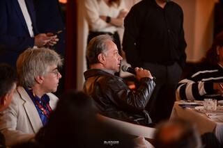 Un hombre está sentado en una silla hablando por un micrófono.