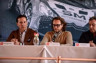 Tres hombres están sentados en una mesa frente a un cartel que dice SM Motorsports.