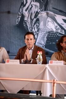 Un hombre está sentado en una mesa con las manos cruzadas delante de un coche.