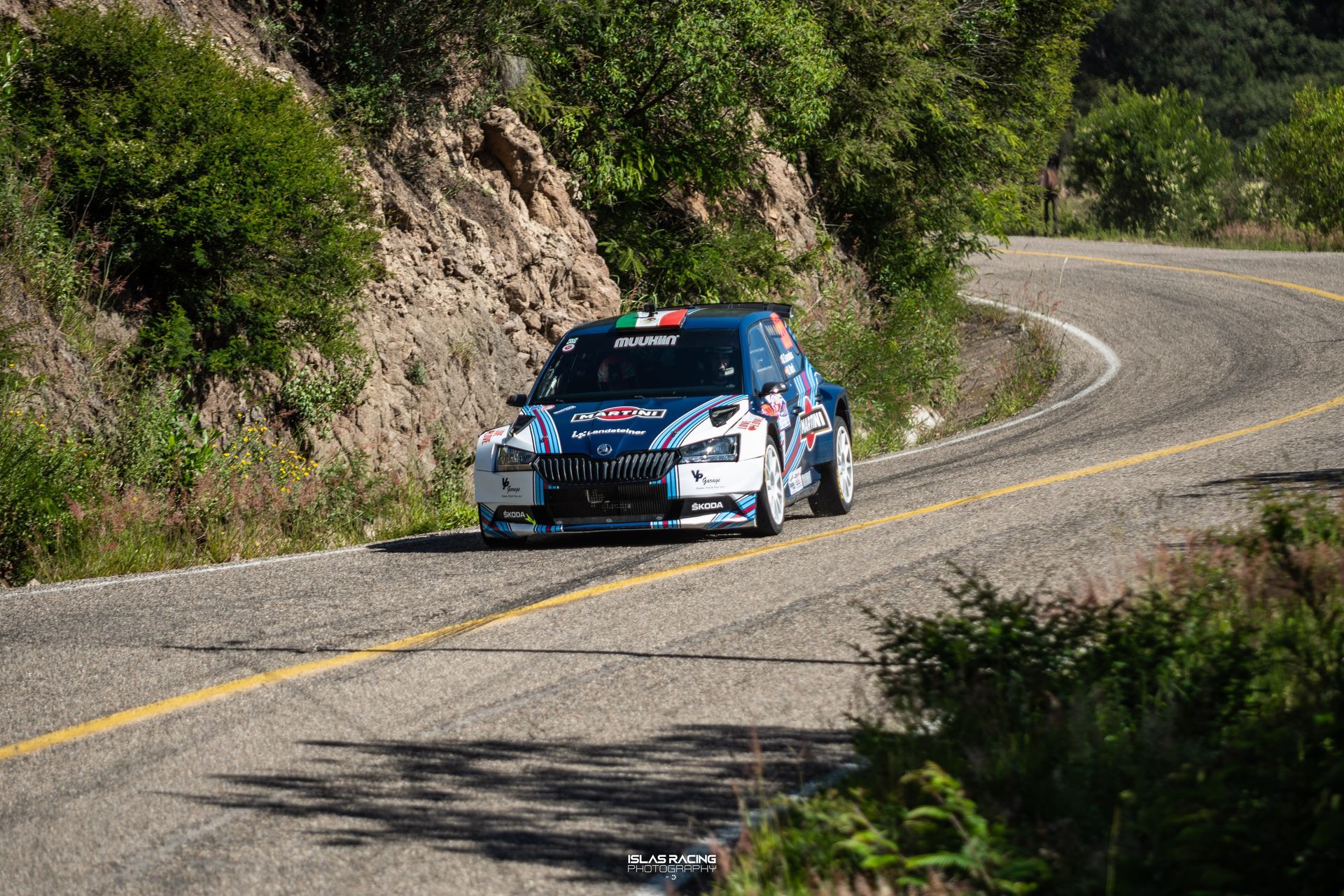 Un coche de rally azul y blanco circula por una carretera con curvas.