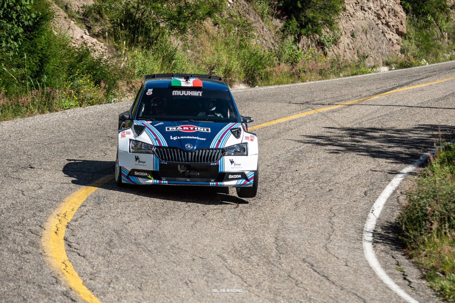 Un coche azul y blanco circula por una carretera con curvas.