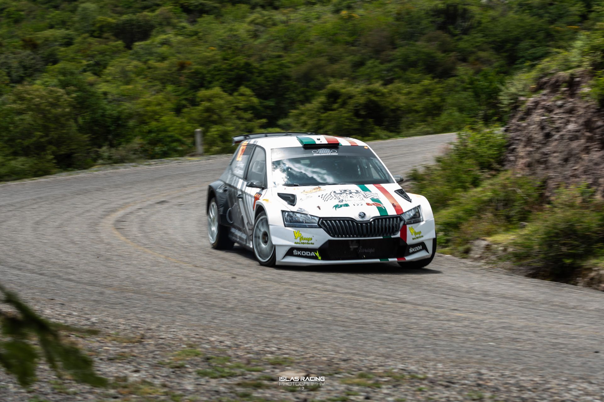 Un coche de rally blanco circula por un camino de tierra.