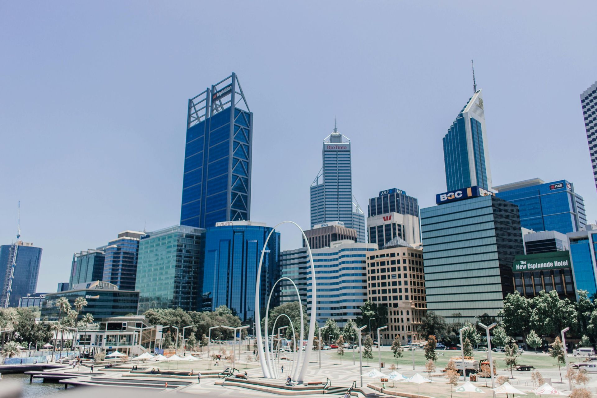 Modern city skyline with tall glass skyscrapers and a waterfront promenade under a clear sky