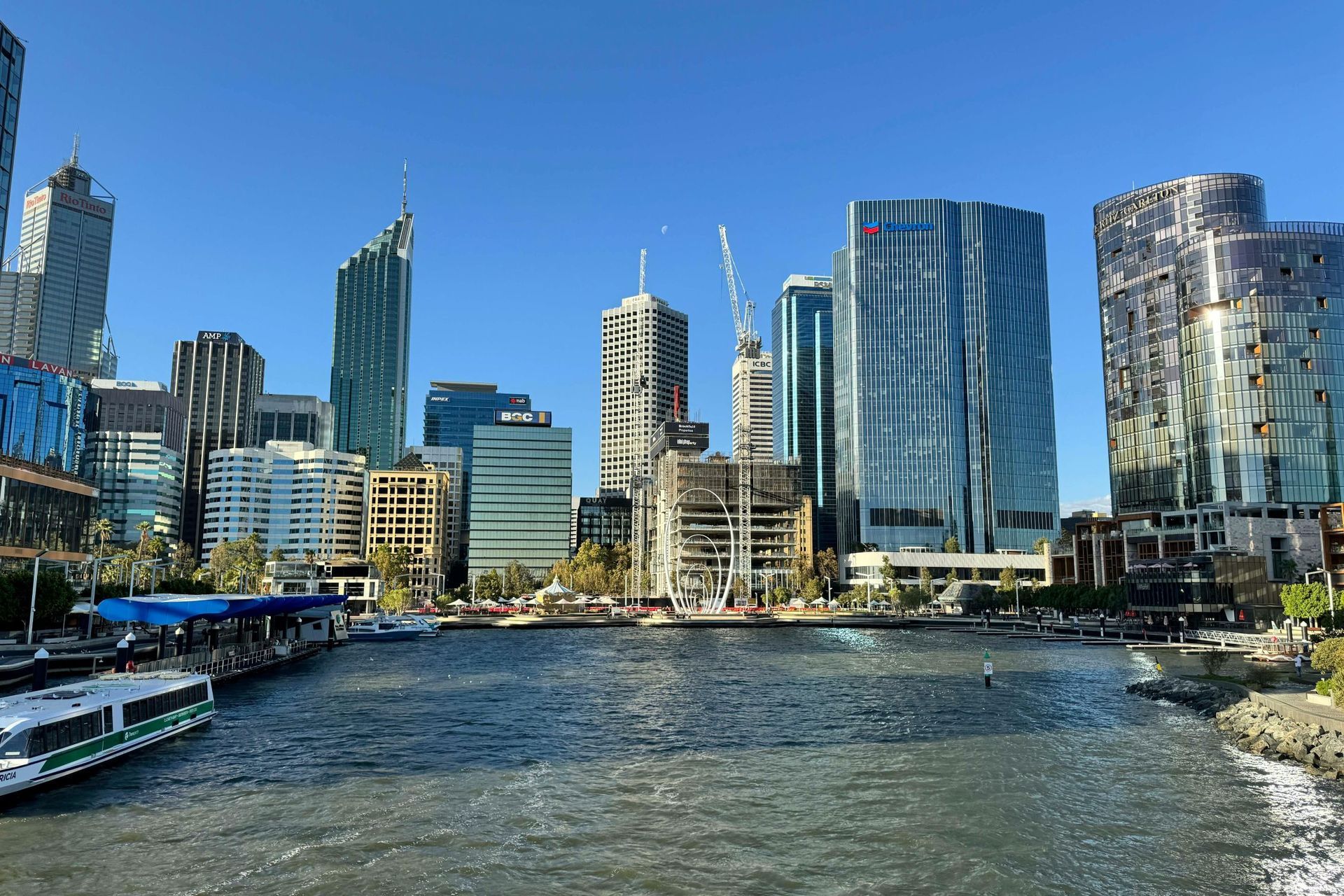 City skyline along a river on a clear day, with modern glass towers and boats in the foreground