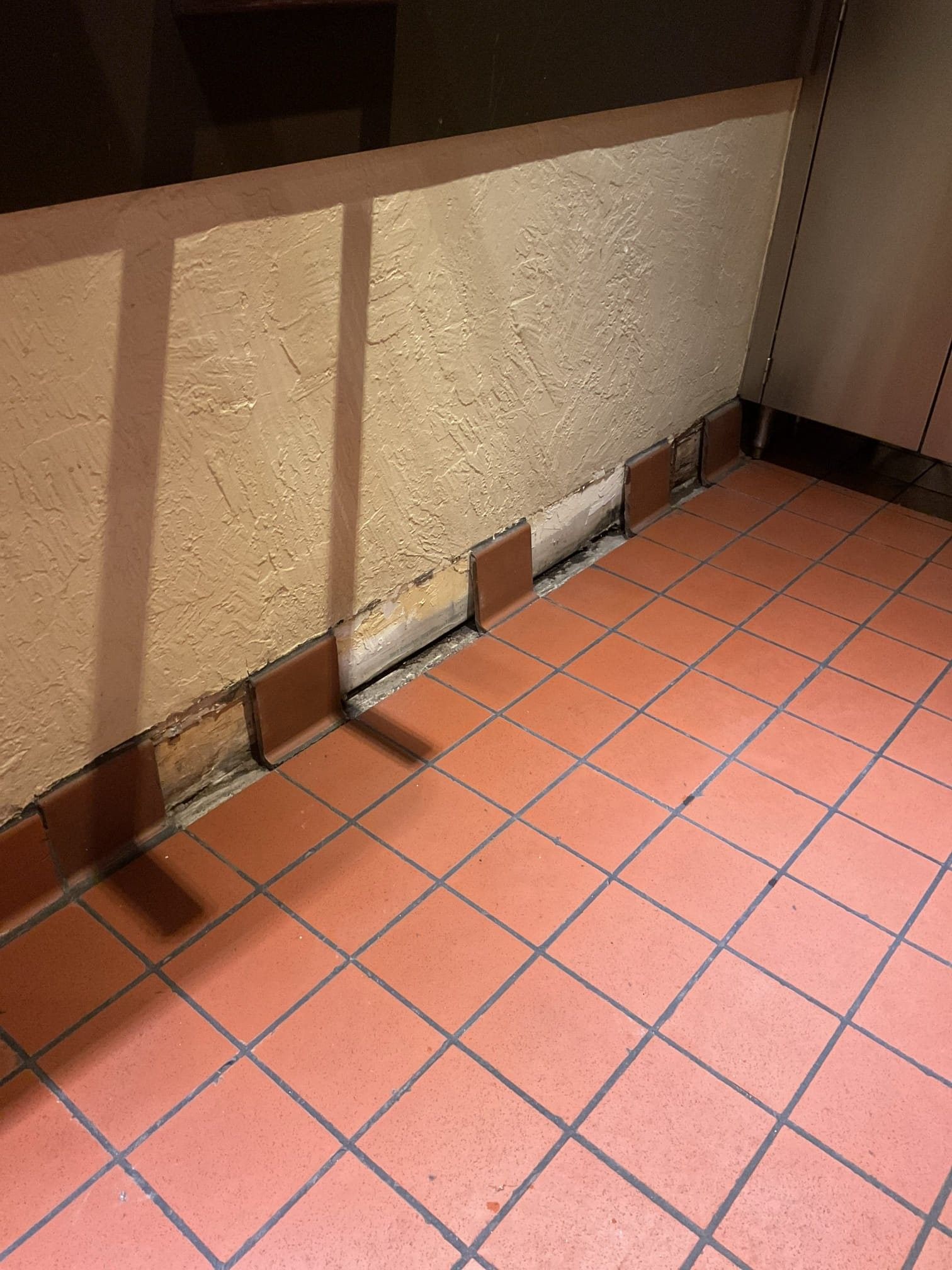 Red tiled floor and wall with missing tiles exposing wood and cement.