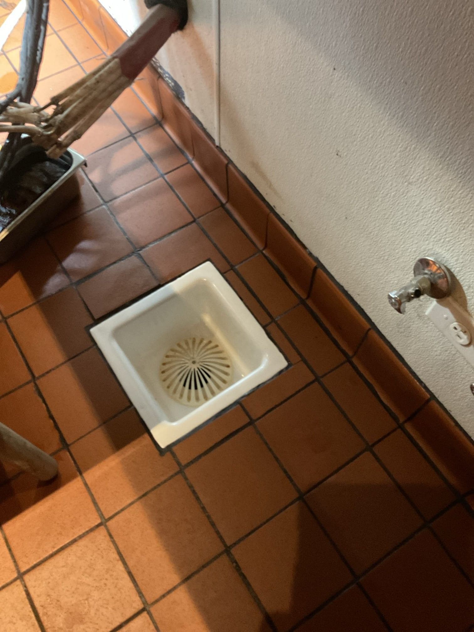 White floor drain on a tiled floor near a faucet and wall.