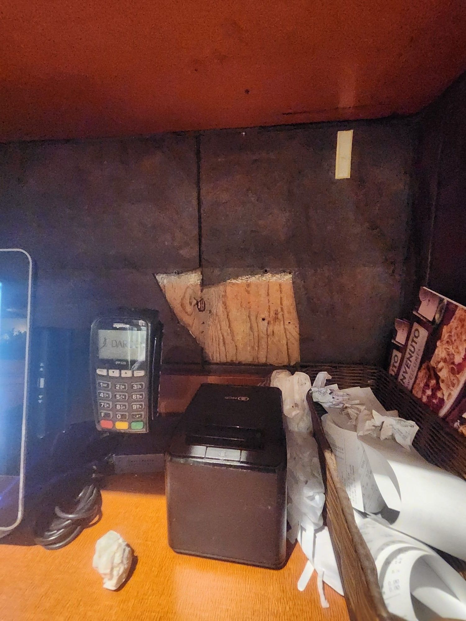 Cash register area with payment terminal, receipts, and a small, white sculpture on the counter.