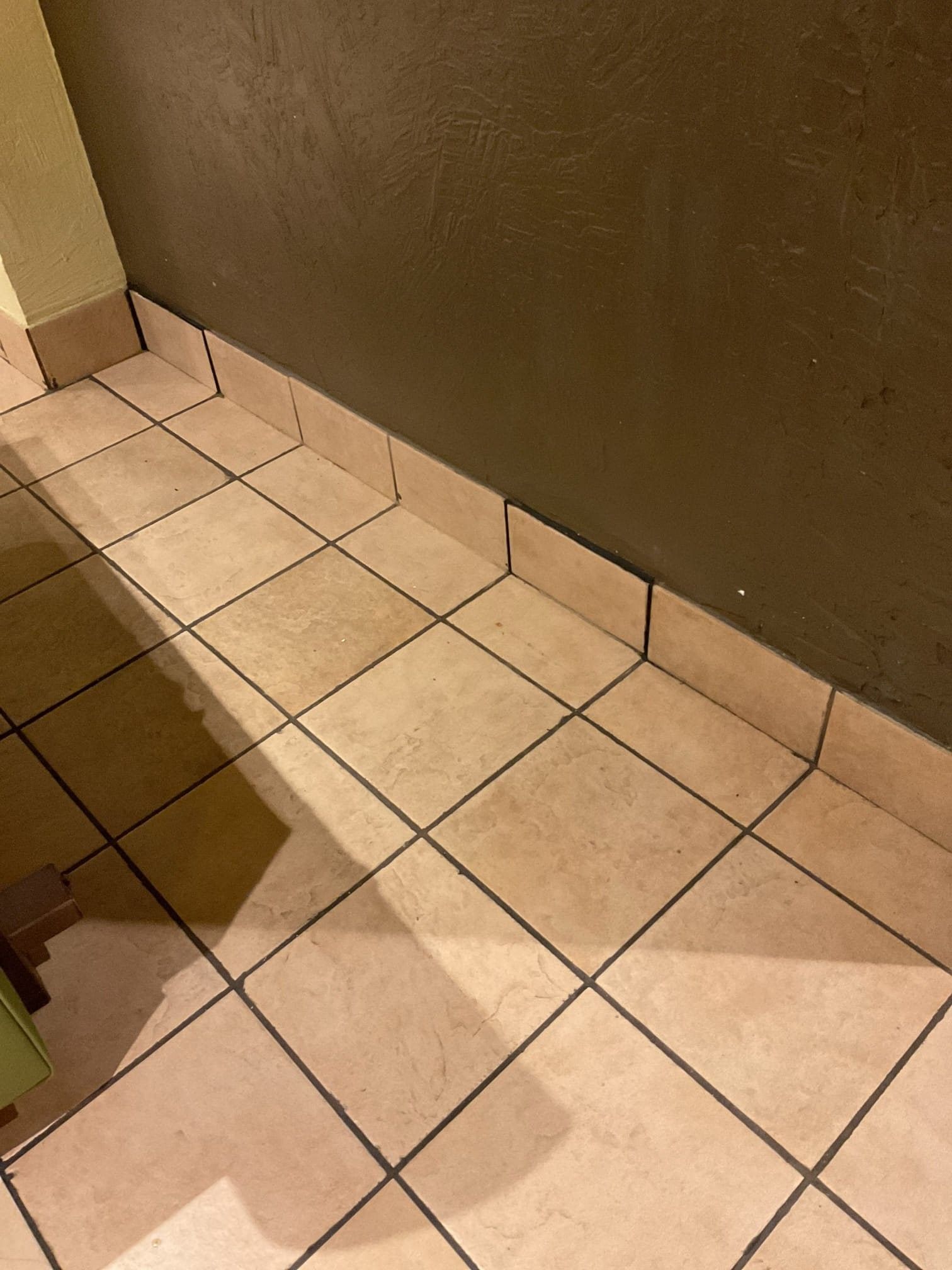 Tan tiled floor meeting a brown wall; dark grout lines.
