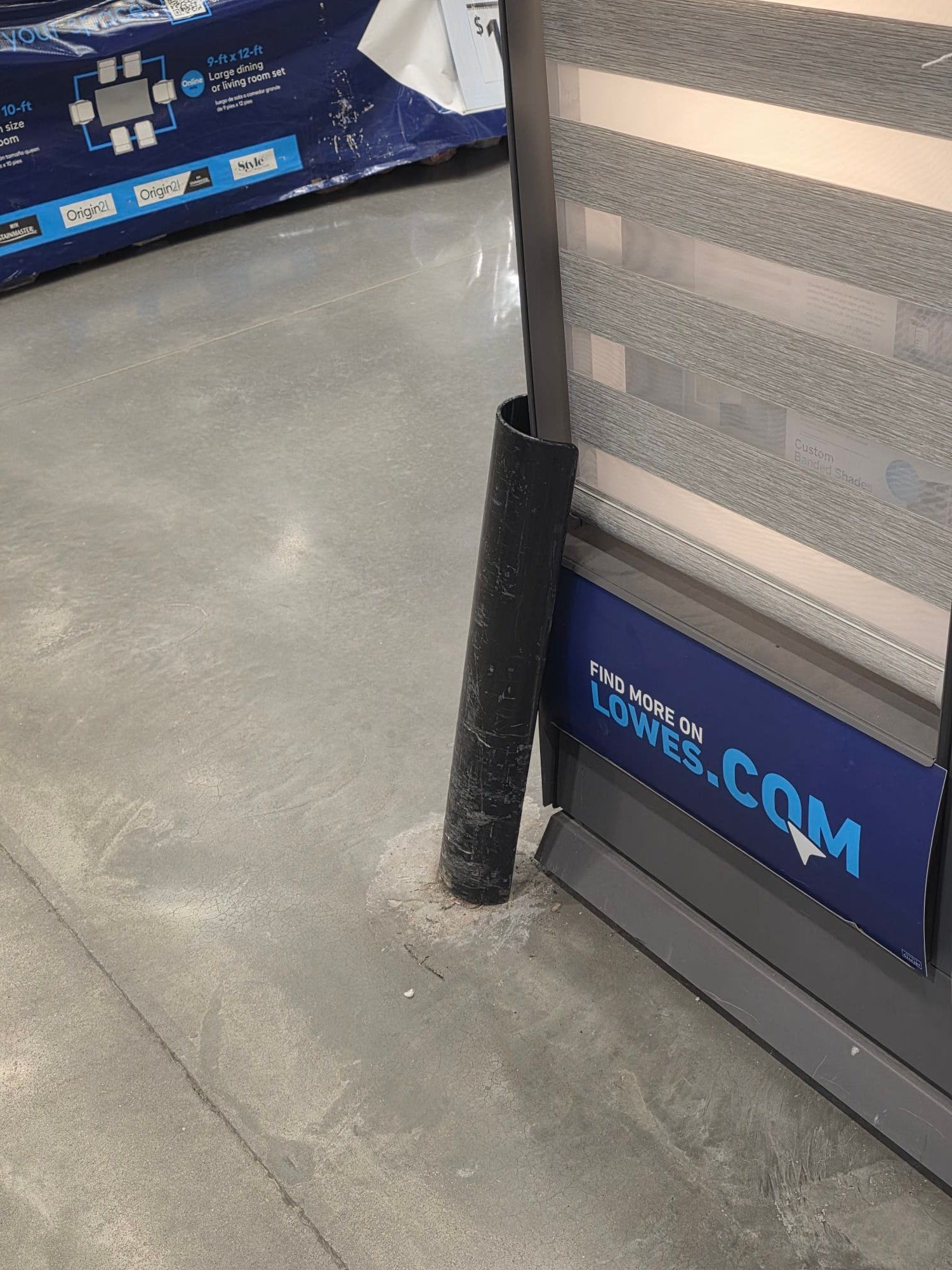 A black pole with a protective sleeve is next to a display with a Lowe's sign, set on a concrete floor.