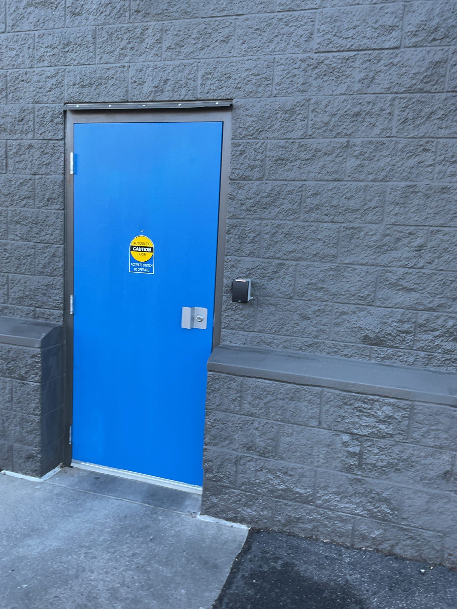 Blue door set in a gray textured wall with an automatic door sticker and accessible push button.