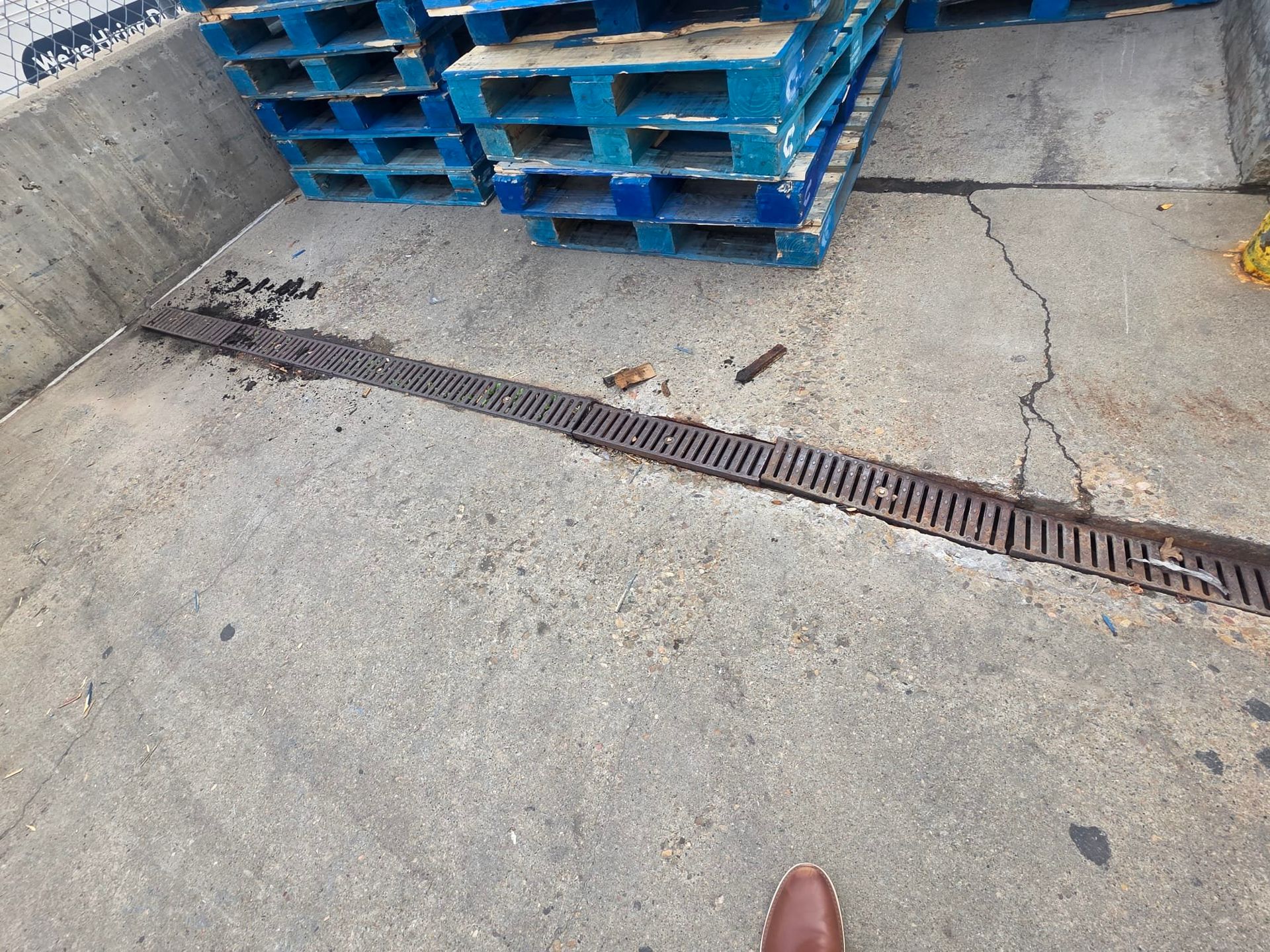 Concrete area with pallets, a long grate, and brown sludge.