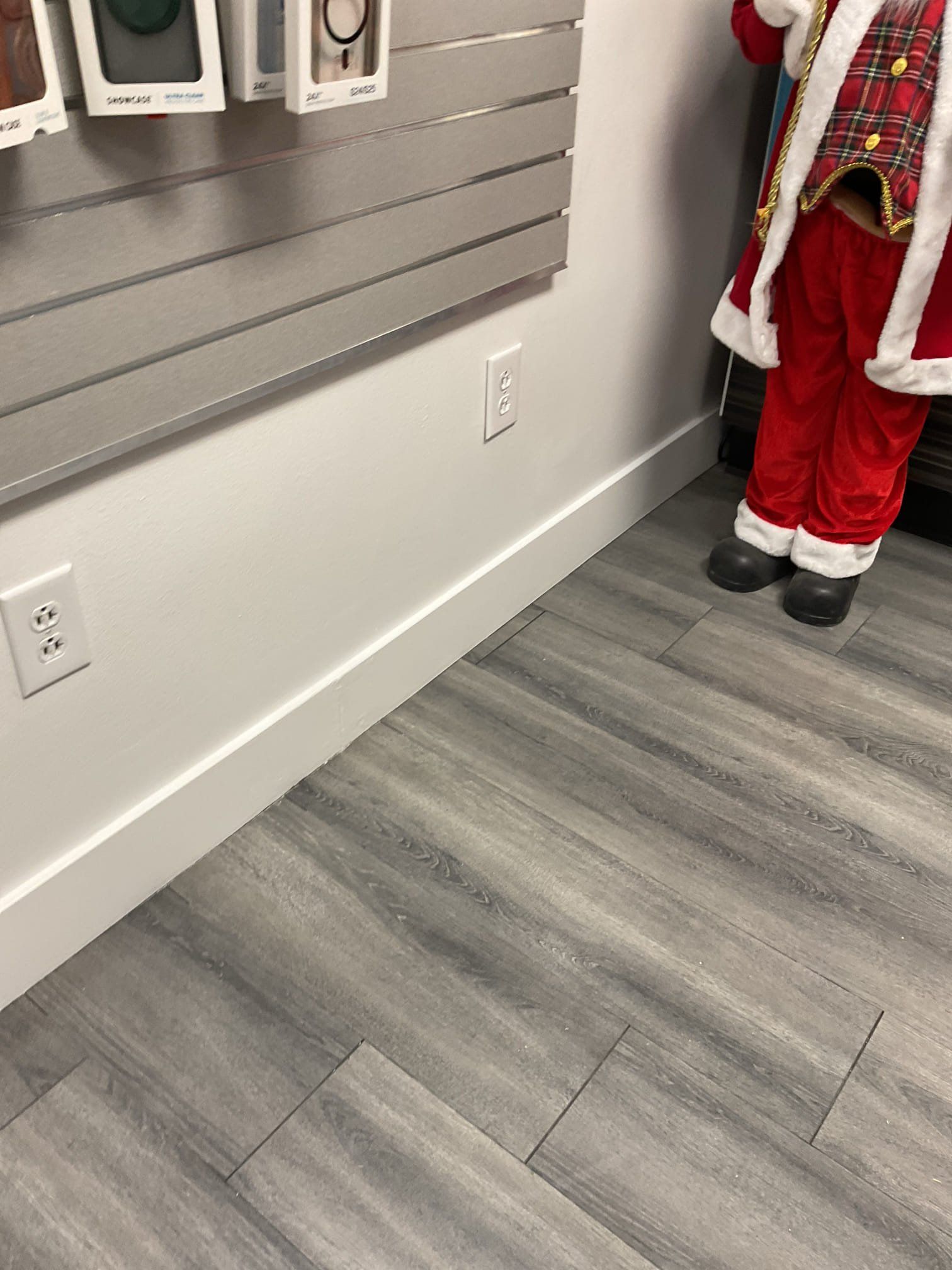 Gray wood-look floor, white wall with electrical outlets, and a Santa Claus figure on the right.