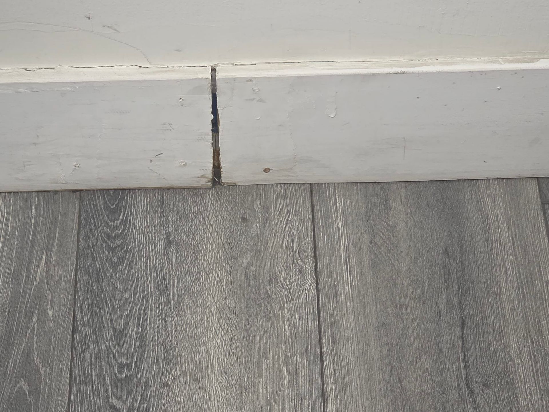 Dirty kitchen floor with a floor drain. Brown tiles, white walls, and pipes.