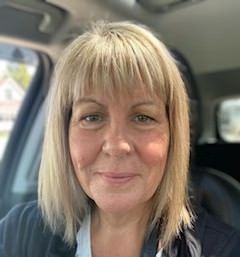 A woman with blonde hair is sitting in a car and smiling.