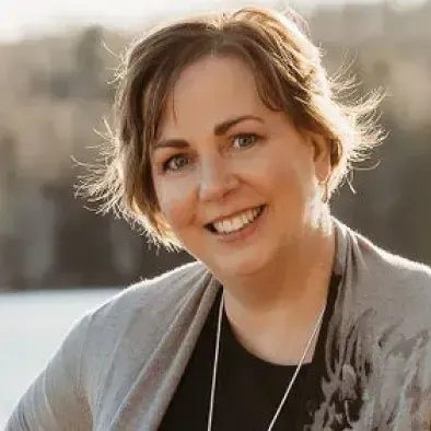 A woman is smiling for the camera while standing next to a body of water.