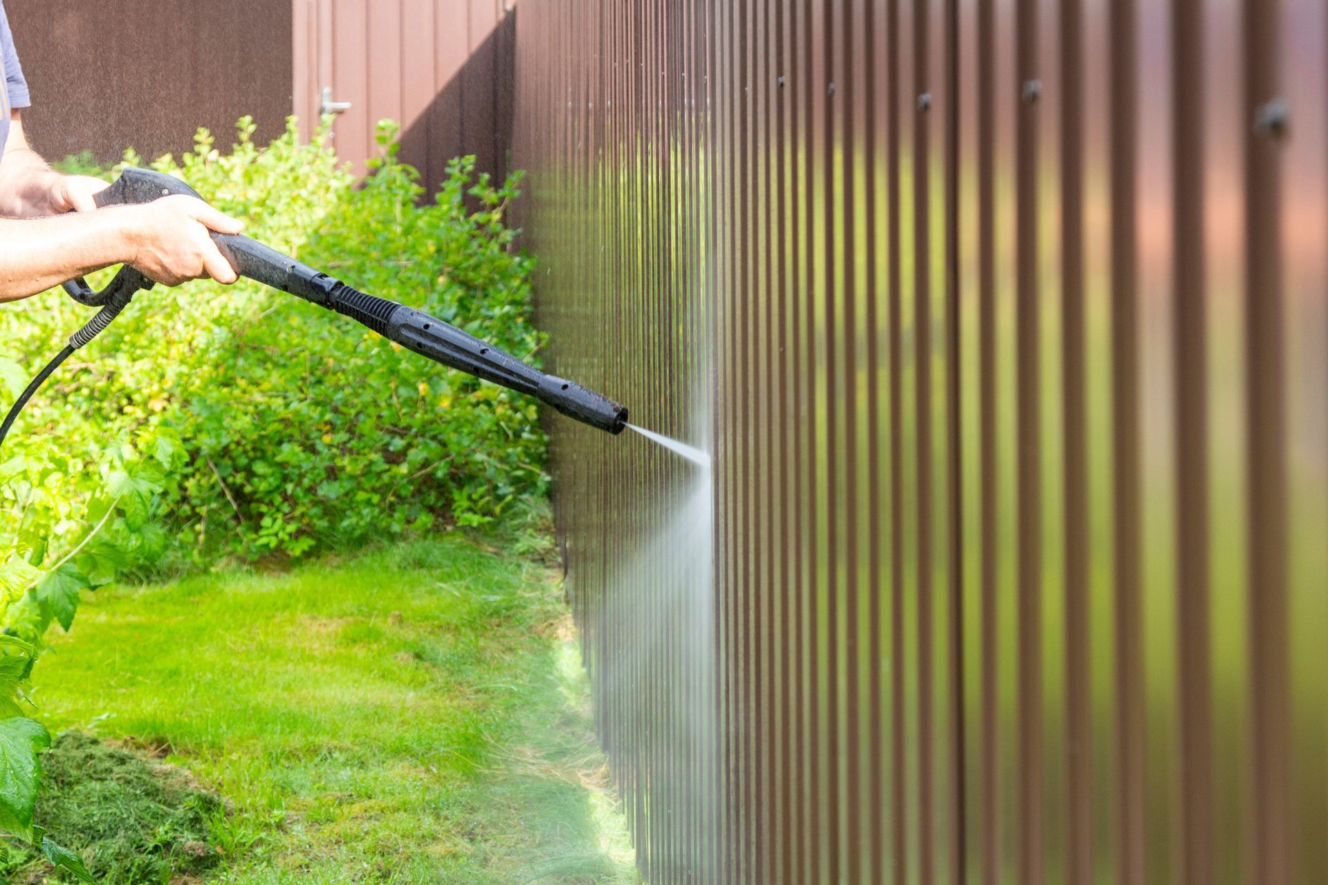 A man is using a high pressure washer to clean a fence.