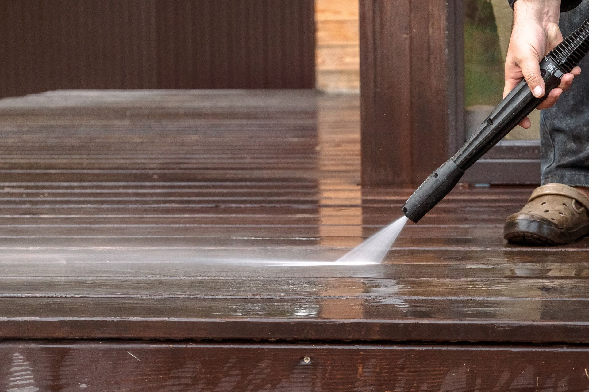 A person is using a high pressure washer to clean a wooden deck.