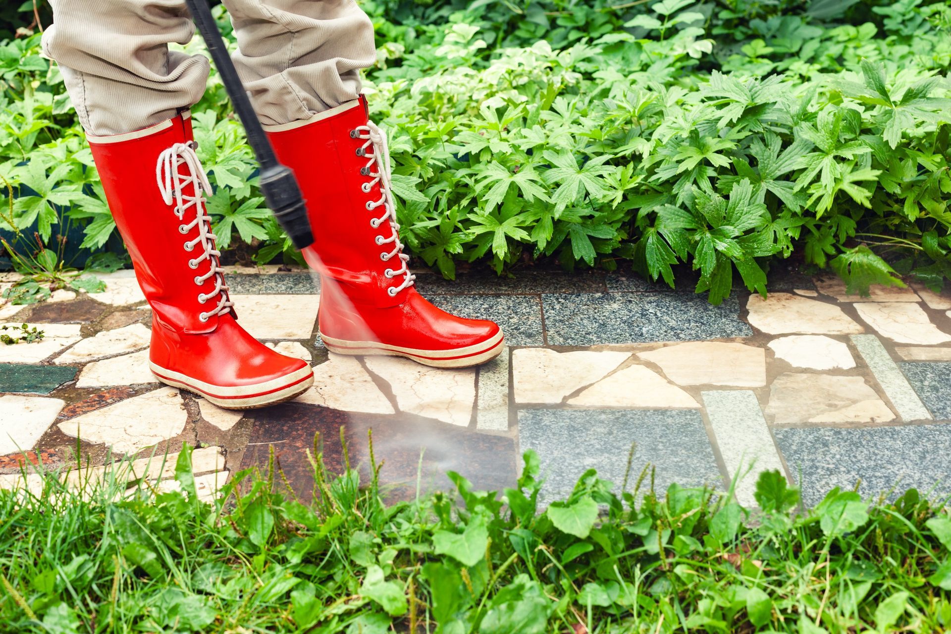 A person wearing red boots is cleaning a sidewalk with a high pressure washer.