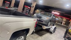 A car is being towed by a truck at a gas station.