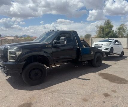 A black tow truck is towing a white car in a parking lot.
