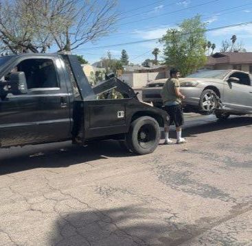 A man is standing next to a tow truck that is towing a car.
