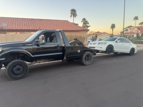 A black tow truck is towing a white car in a parking lot.