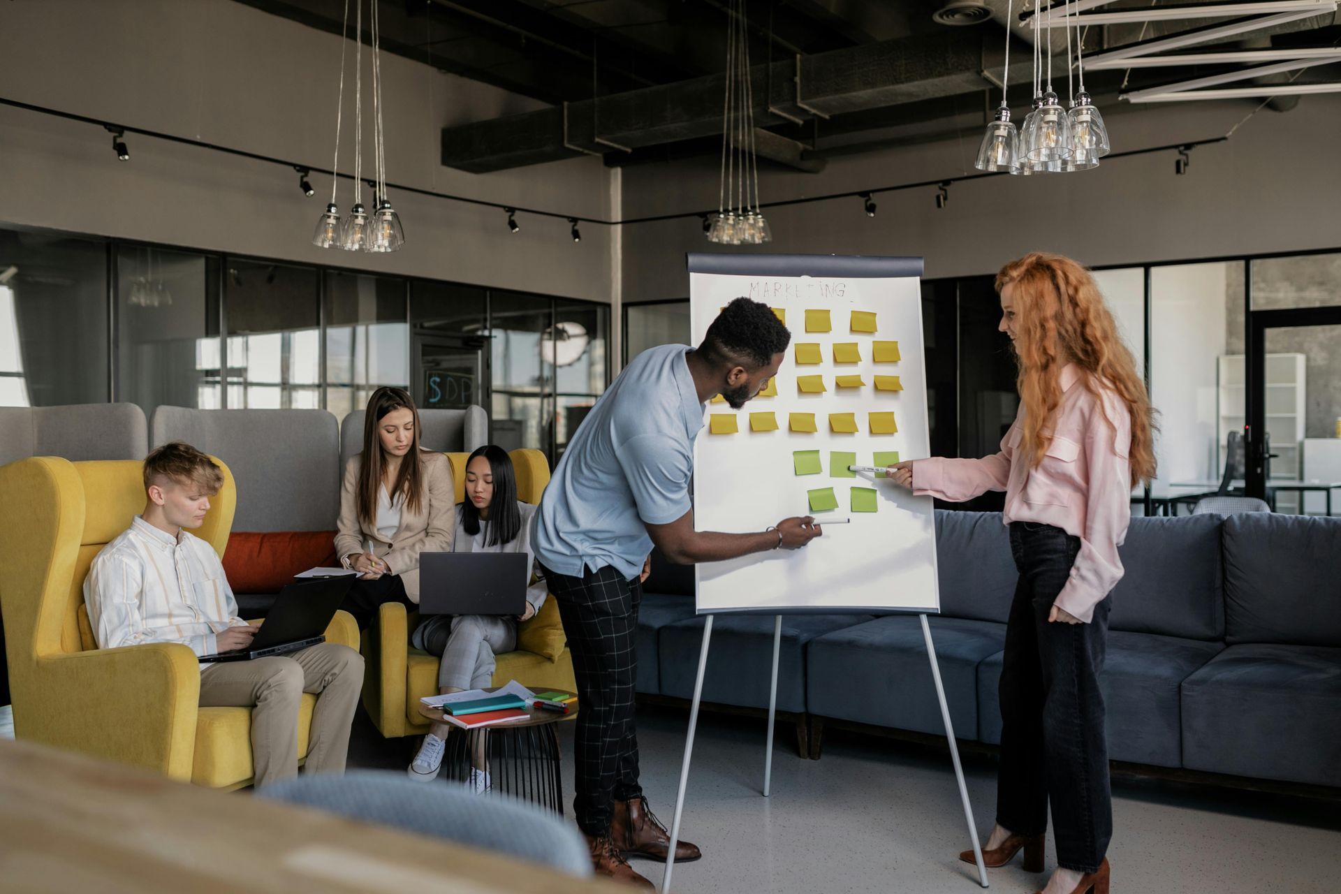 Group of colleagues collaborating around a whiteboard with sticky notes in a modern office space.