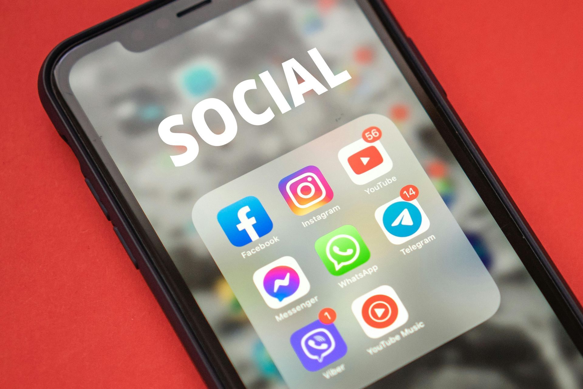Smartphone displaying social media app icons, including Facebook, Instagram, YouTube, and WhatsApp, on a red background.