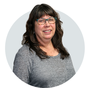 A woman wearing glasses and a grey shirt is smiling in a circle.