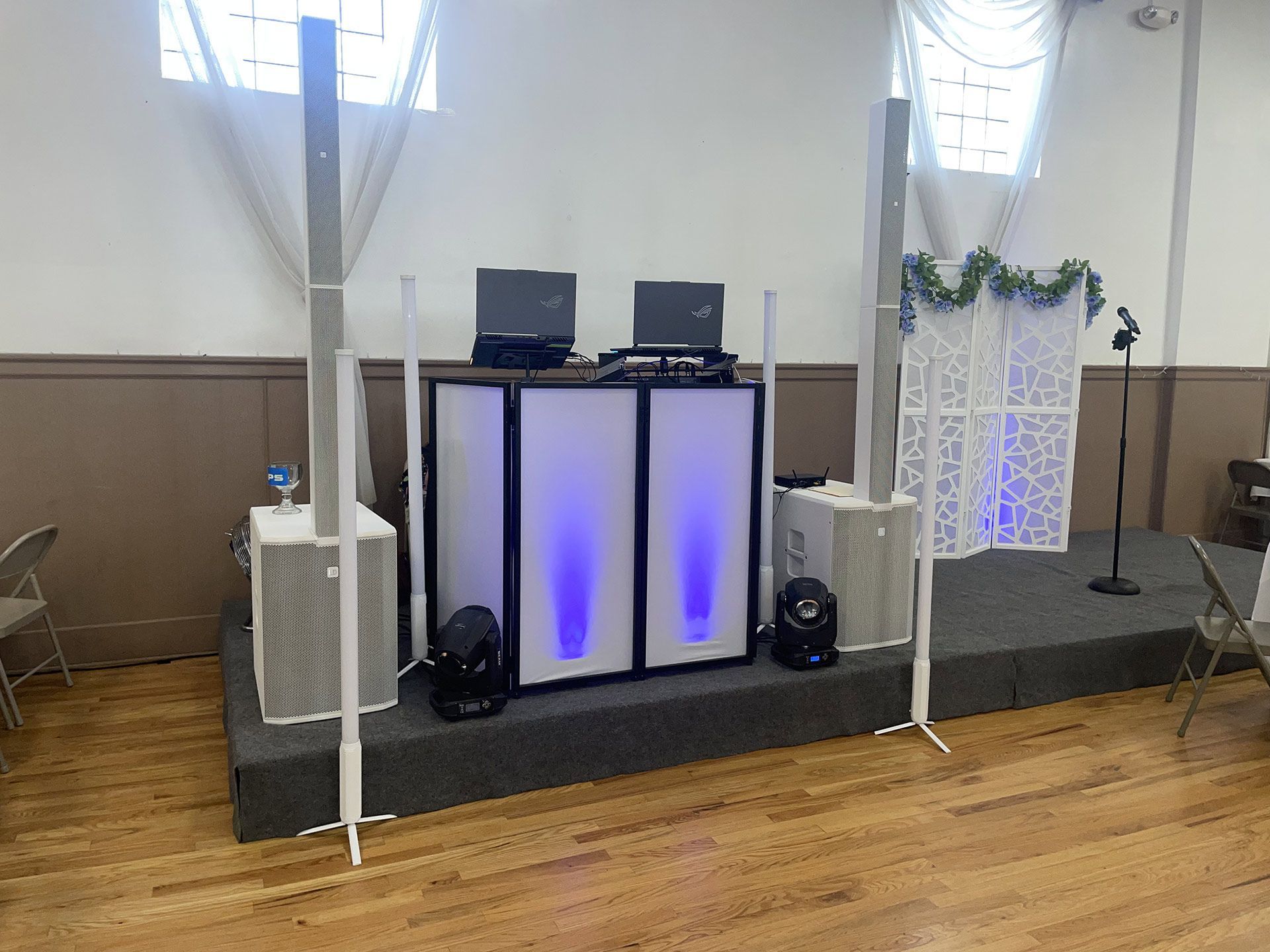 DJ setup with speakers, lights, and a laptop on a small stage in a room.