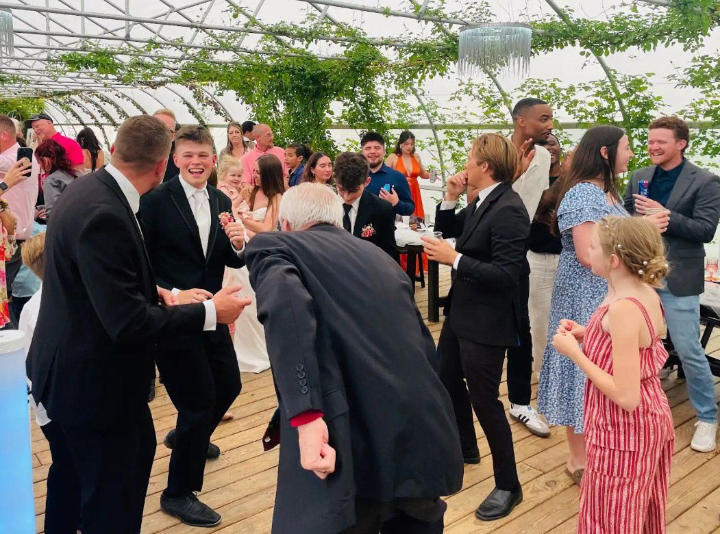 People dancing at a wedding reception in a bright, open tent.