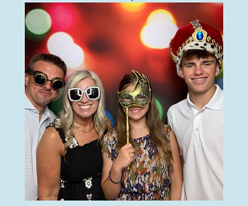 Family of four in photo booth posing with props.