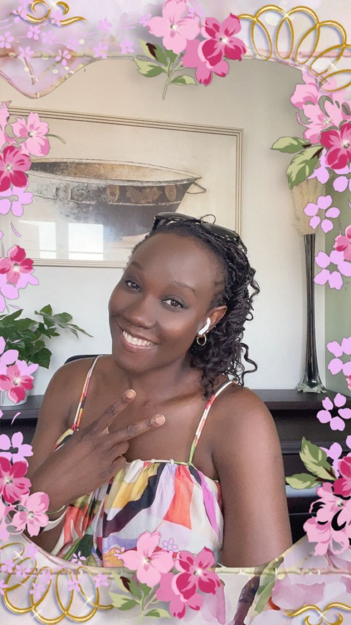 A woman is smiling in front of a mirror surrounded by pink flowers.