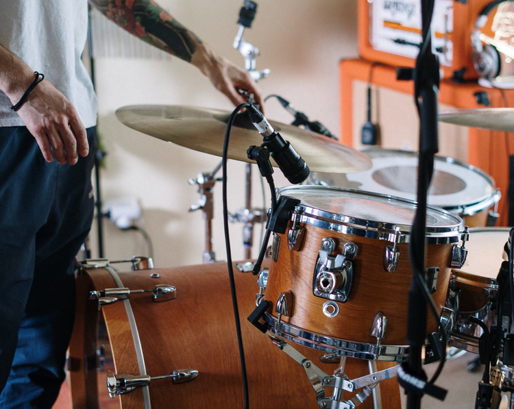 A drum set with a microphone over it, with a tattooed man adjusting it.