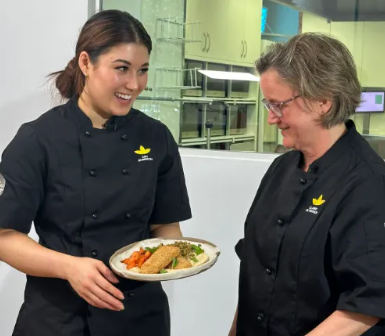 A woman in a chef 's uniform is holding a plate of food