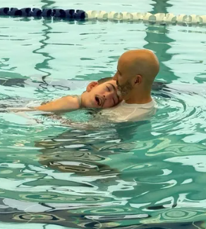 A man is holding a child in a swimming pool
