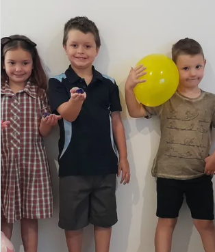 Three children standing next to each other with one holding a yellow balloon