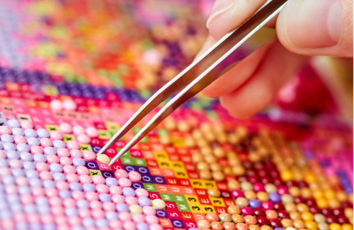 A person is holding tweezers over a diamond painting.