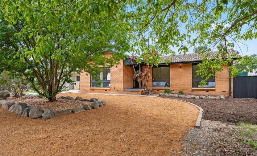 A brick house with a gravel driveway and a tree in front of it.