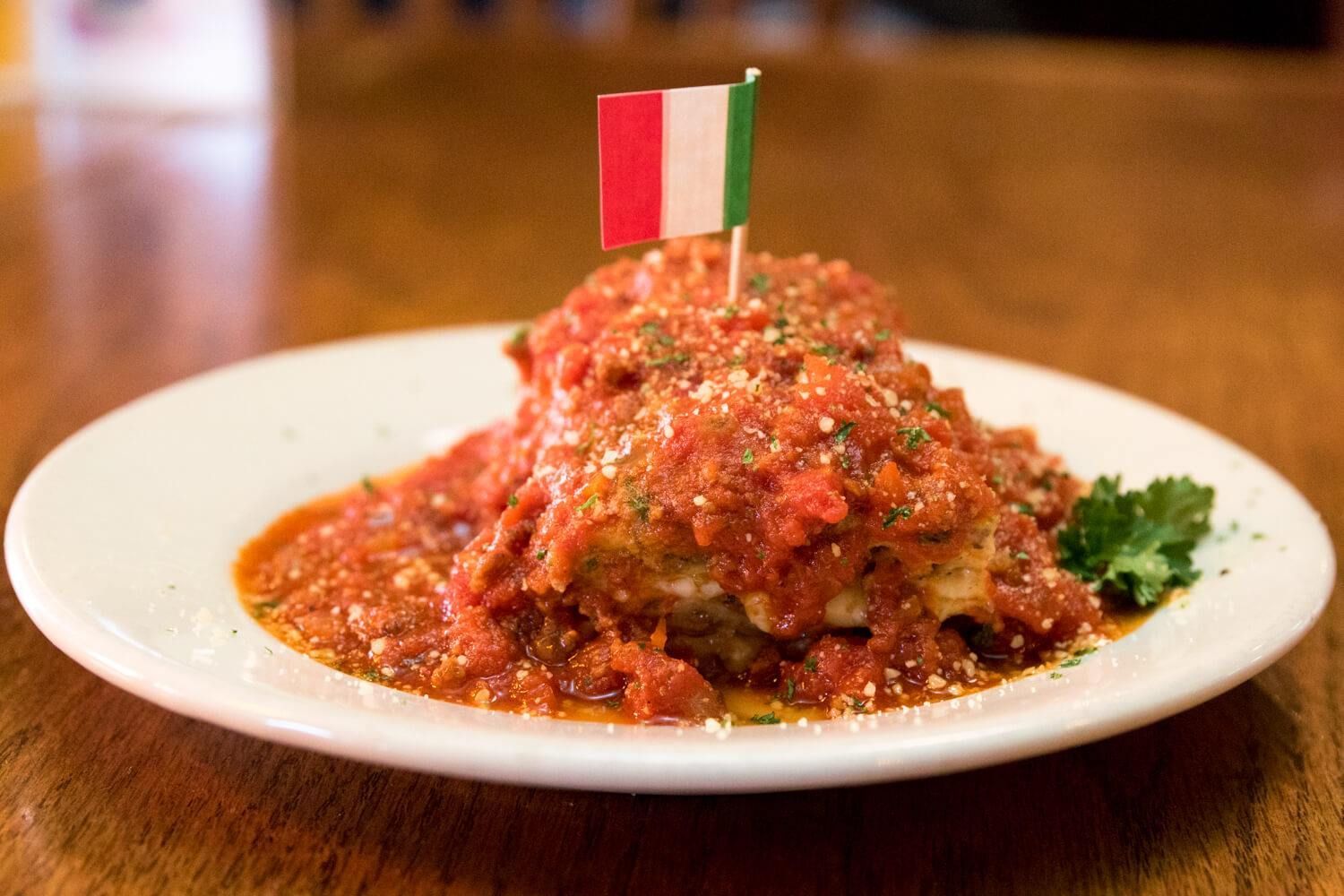 Lasagna topped with red sauce, Italian flag, served on white plate.