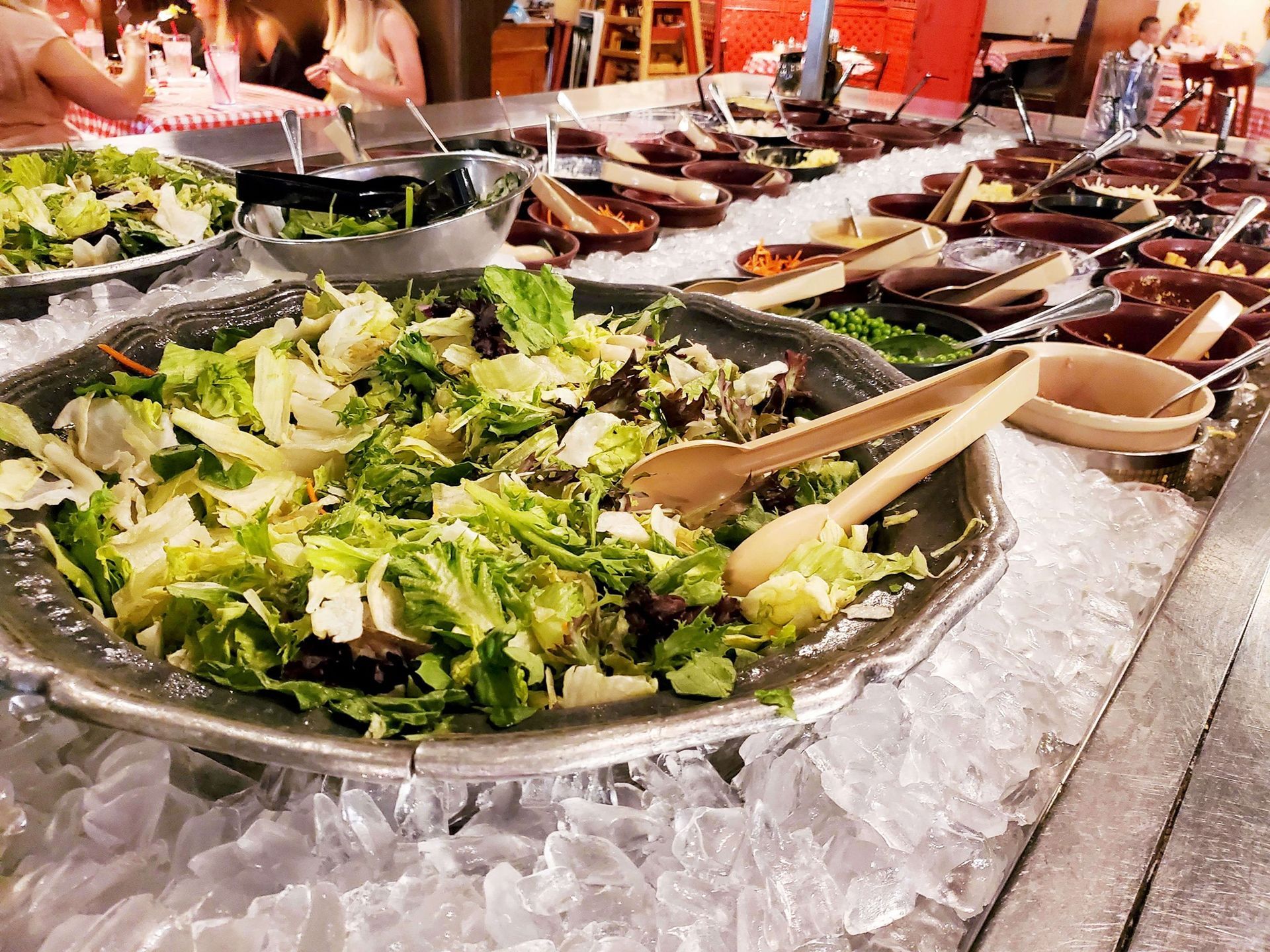 Salad bar with large silver platter of lettuce, other food trays, and tongs, resting on ice.