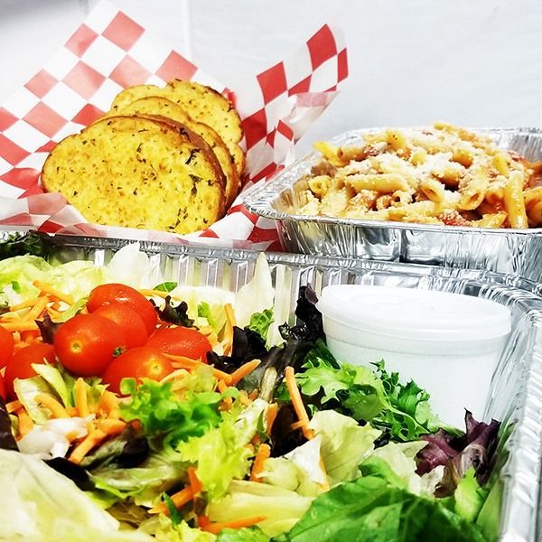 Meal with pasta, salad with tomatoes, garlic bread on checkered paper, and dipping sauce in foil containers.