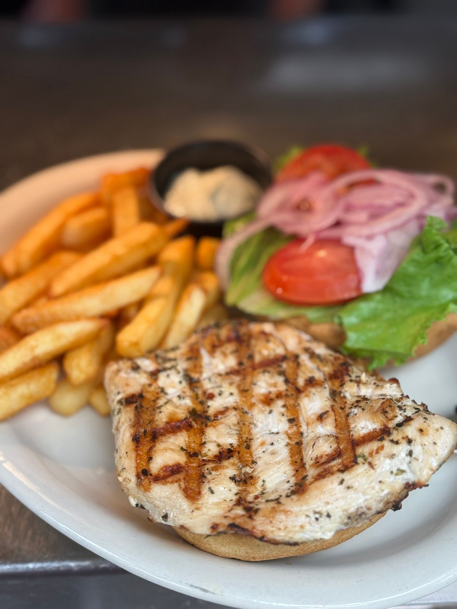 Grilled chicken sandwich with fries and dipping sauce.